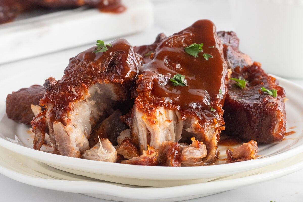 A plate of tender, saucy barbecue ribs garnished with chopped parsley, with a rich glaze and juicy, pulled meat visible.