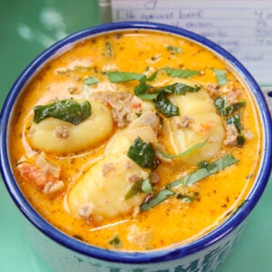 Creamy soup with gnocchi, ground meat, tomatoes, and spinach in a blue and white mug. A handwritten recipe card is slightly visible in the background.
