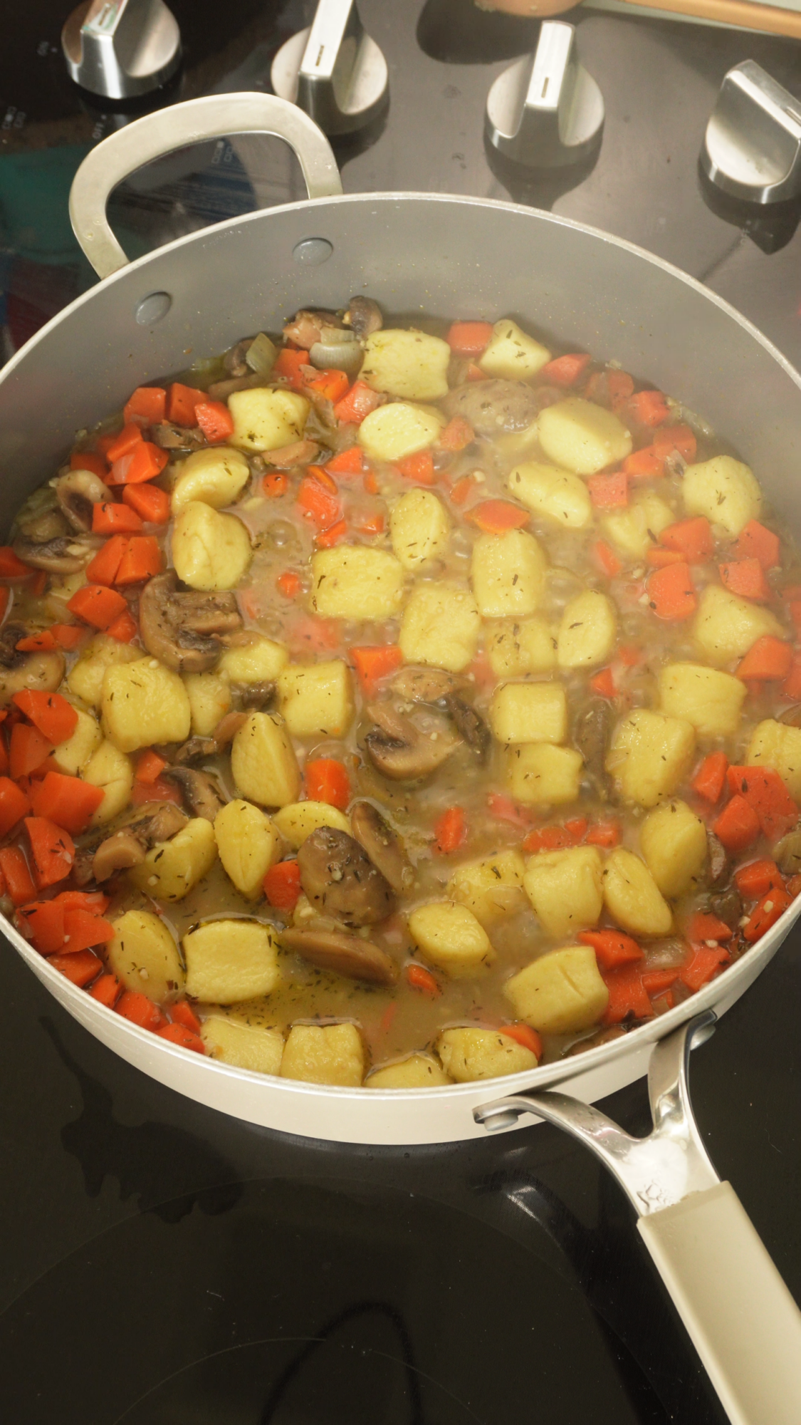 A pot of diced potatoes, carrots, and mushrooms cooking in broth on a stovetop, with steam rising from the mixture.