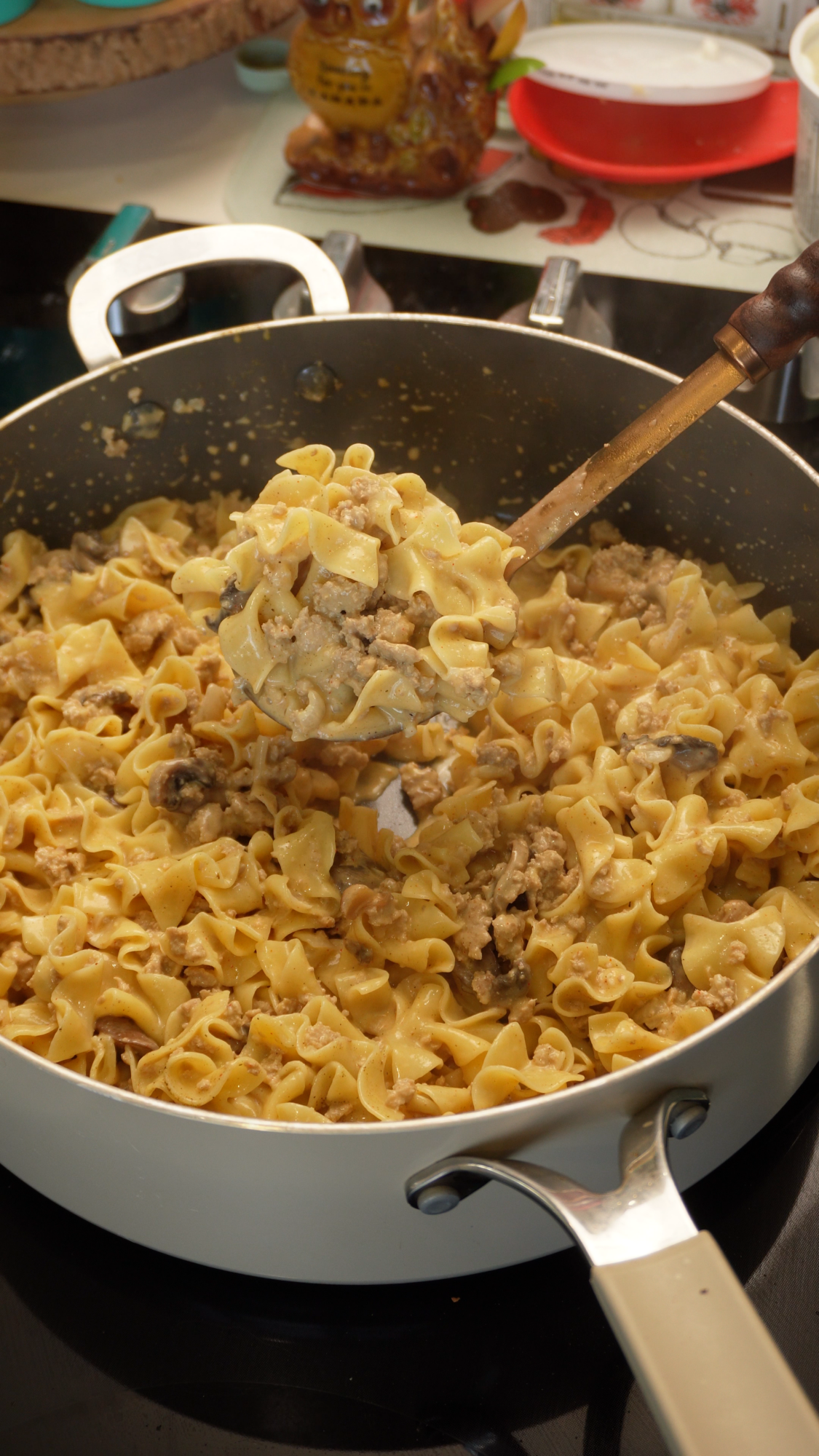 A ladle lifts a portion of creamy beef and noodle stroganoff from a large pan.