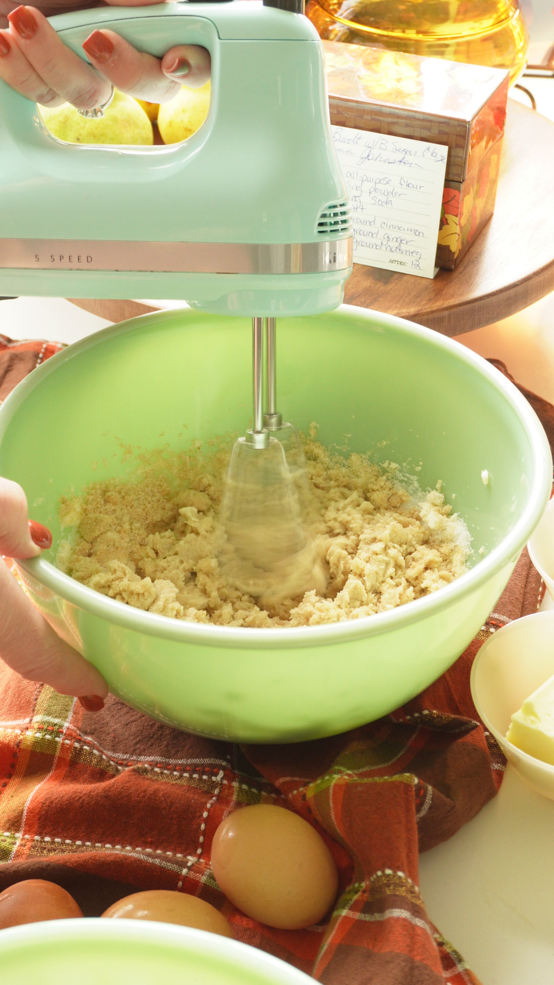 A hand holds a mint green electric hand mixer beating dough in a matching green mixing bowl.