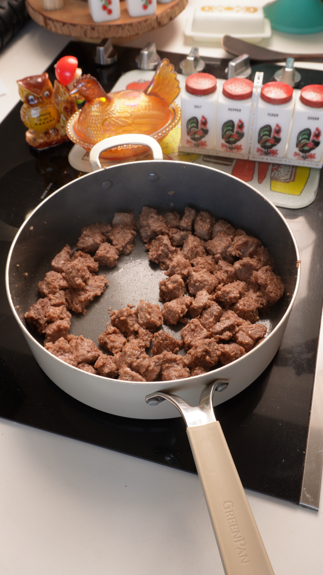 Small, browned pieces of meat cooking in a light-colored skillet on a stovetop.