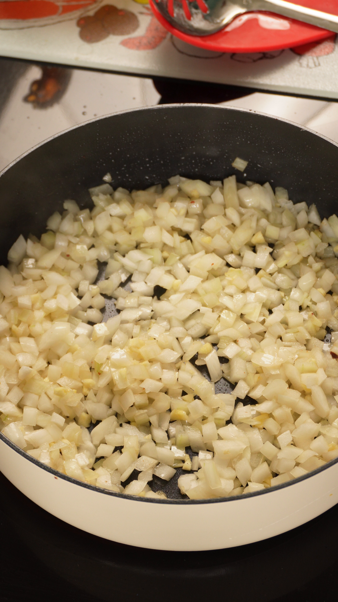 Diced onions and garlic sautéing in a skillet on a stovetop.